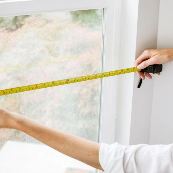 Hands measuring a window with a tape measure